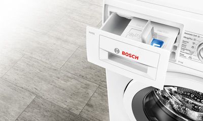 Weißer, freistehender Kühlschrank mit Griff an der Seite, vor einer Wand mit diagonal gestreiftem Muster.